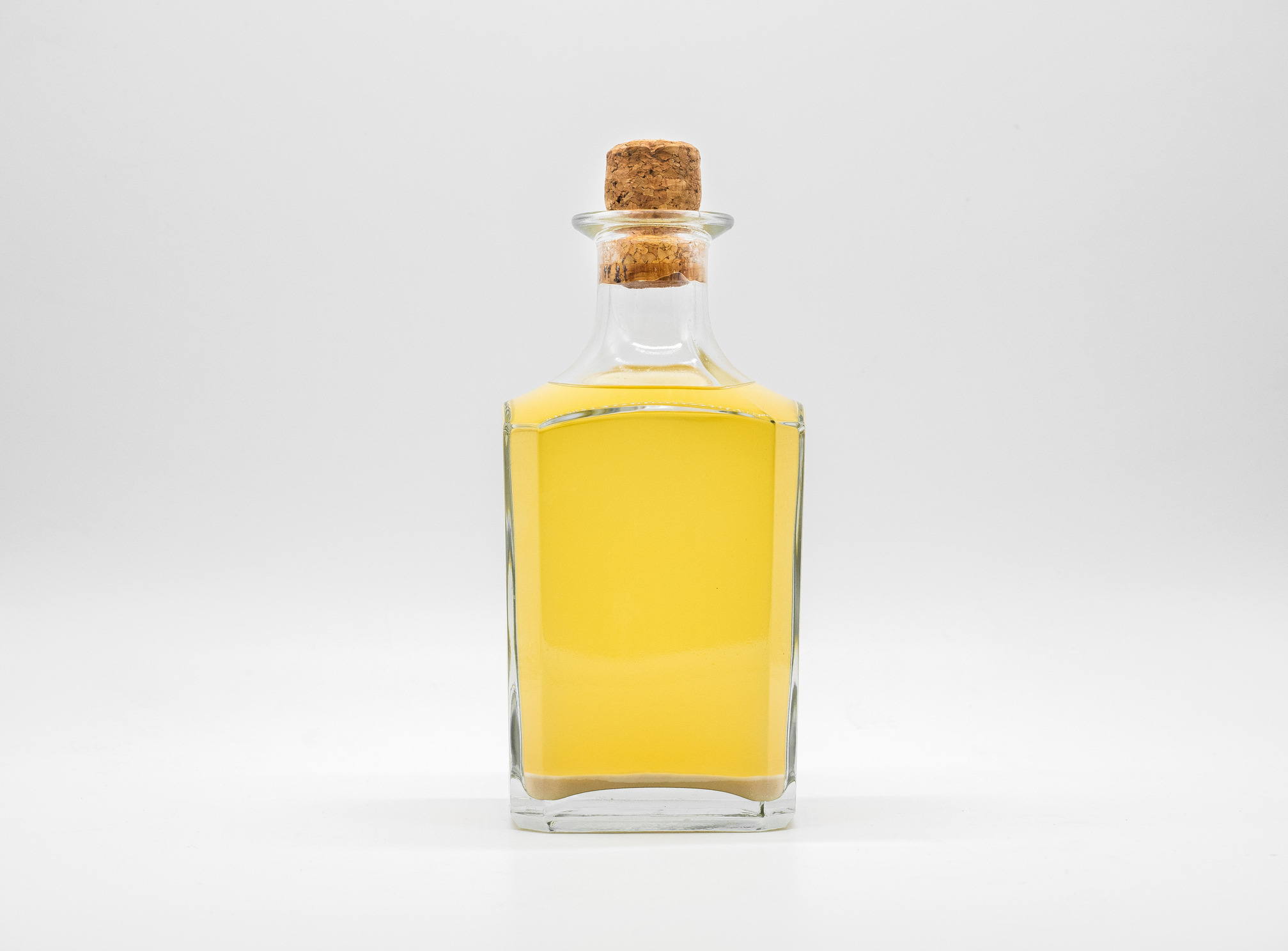 Transparent square bottle with yellow liquid. Front view of the vertical staying jar.